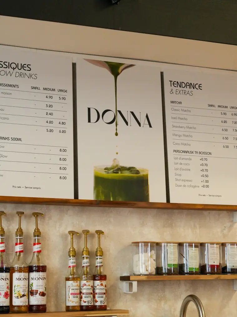 Le comptoir du café : les pancartes de la carte au mur, les sirops et les bocaux sur les étagères de bois
